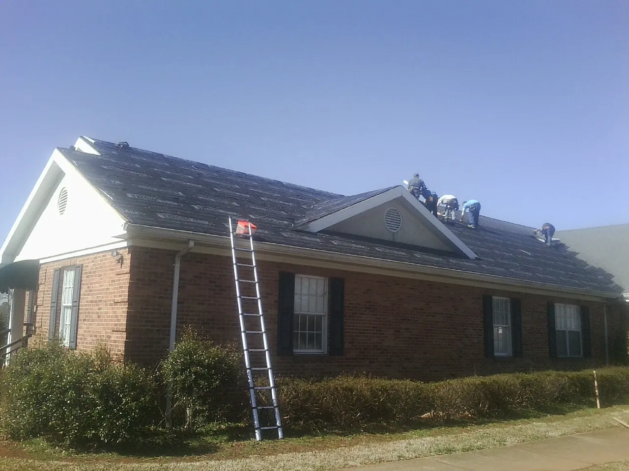Crew tearing shingles off a brick ranch roof with a ladder set — Emergency Roof Repair work by our crew in Creve Coeur