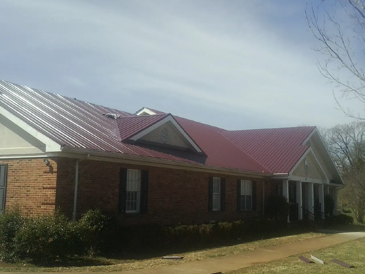 Red metal roof with gabled entries on a long brick building, from a Hail Damage Roof Repair job in Creve Coeur