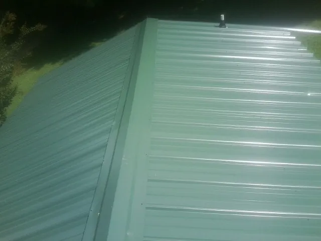 New green metal panels meeting at the ridge of a roof — Flat Roof Repair work by our crew in Creve Coeur