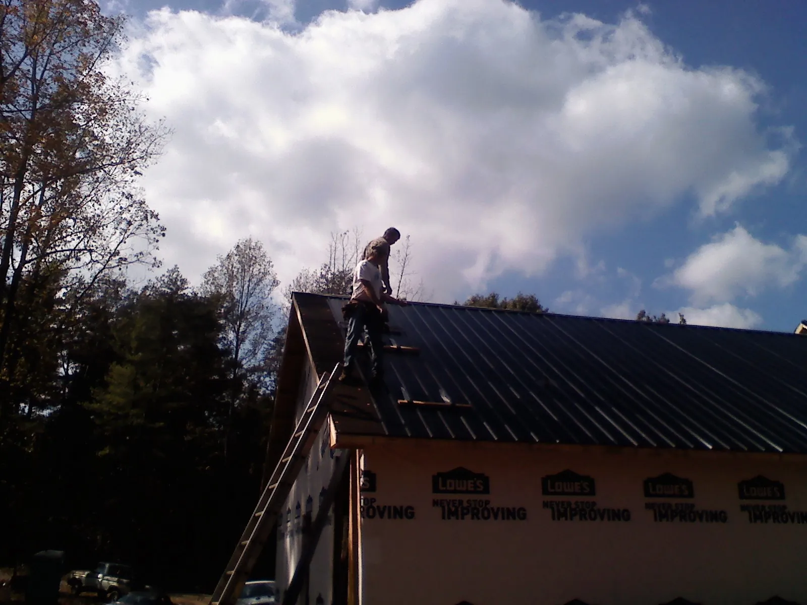 Roofer fastening dark metal panels high against a cloudy sky, from a Roof Inspection job in Creve Coeur