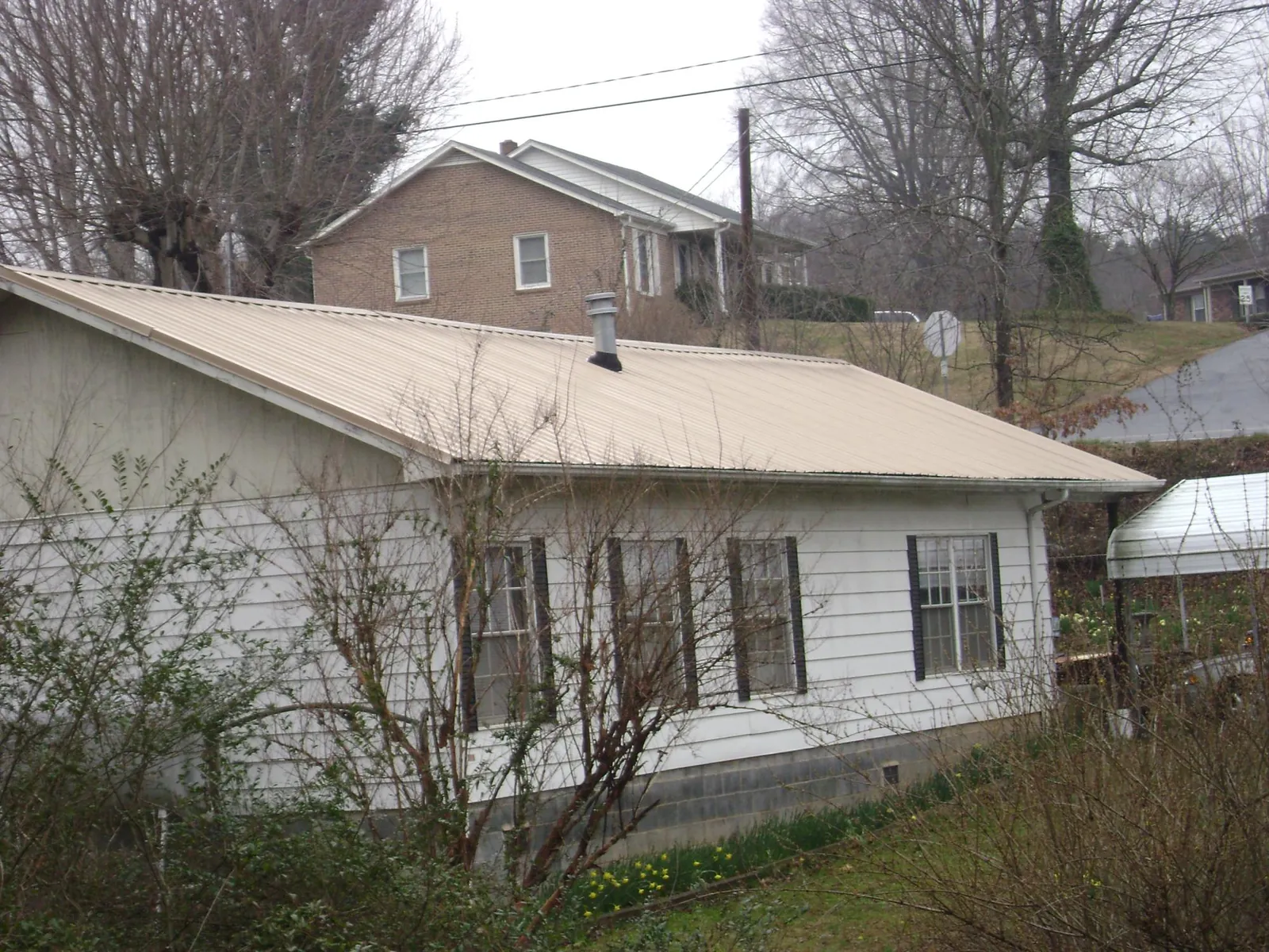 Tan metal roof on a white sided house set into a hillside — Commercial Roofing by Roofing Brothers in Creve Coeur