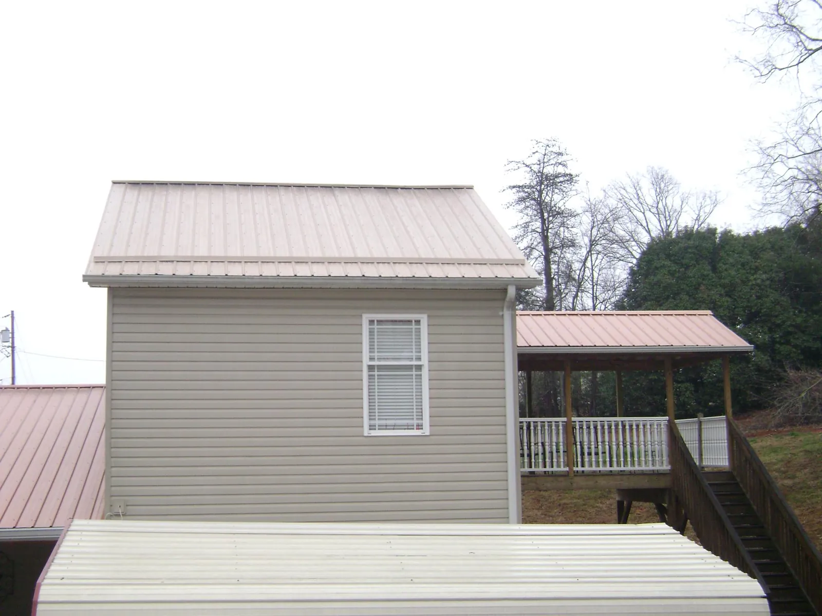 Tan metal roofs on a two story addition and attached porch, from a Roof Replacement job in Creve Coeur